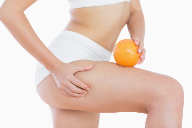 Woman squeezes cellulite skin on thigh as she holds orange
