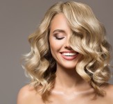 Blonde woman with curly beautiful hair smiling on gray backgroun