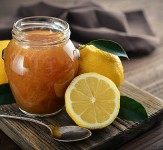Lemon jam in jar with fresh lemons on wooden background closeup